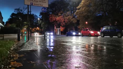 cars-line-on-glossy-road-in-London-at-night-waiting-for-green-signal-light,-ground-level-still-shot