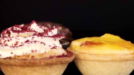 an array of chocolate, custard, and red velvet mini desserts rotates on a black background, illuminated by soft studio lighting with a shallow depth of field