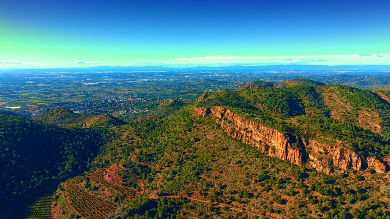 Paisaje aéreo de laderas de montañas y valle de plantaciones de cítricos. Vista aérea de gran angular de montañas verdes con huertos de naranjos en terrazas en el valle durante el día.