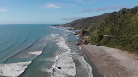 vista de drones de la costa este de nueva zelanda con olas lentas y playa rocosa en un día claro de verano en 4k