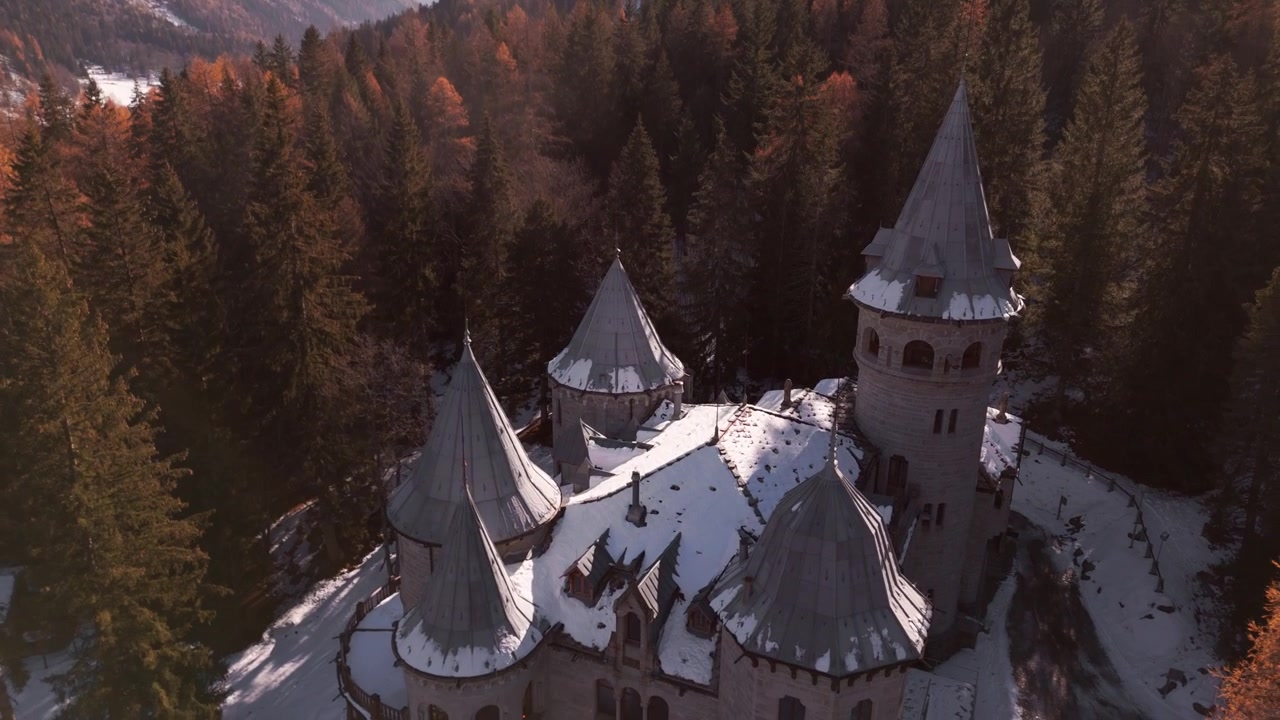 Dron zachycuje hrad Castel Savoia v zimě, jehož věže se tyčí nad zasněženým lesem pod křišťálově čistou alpskou oblohou