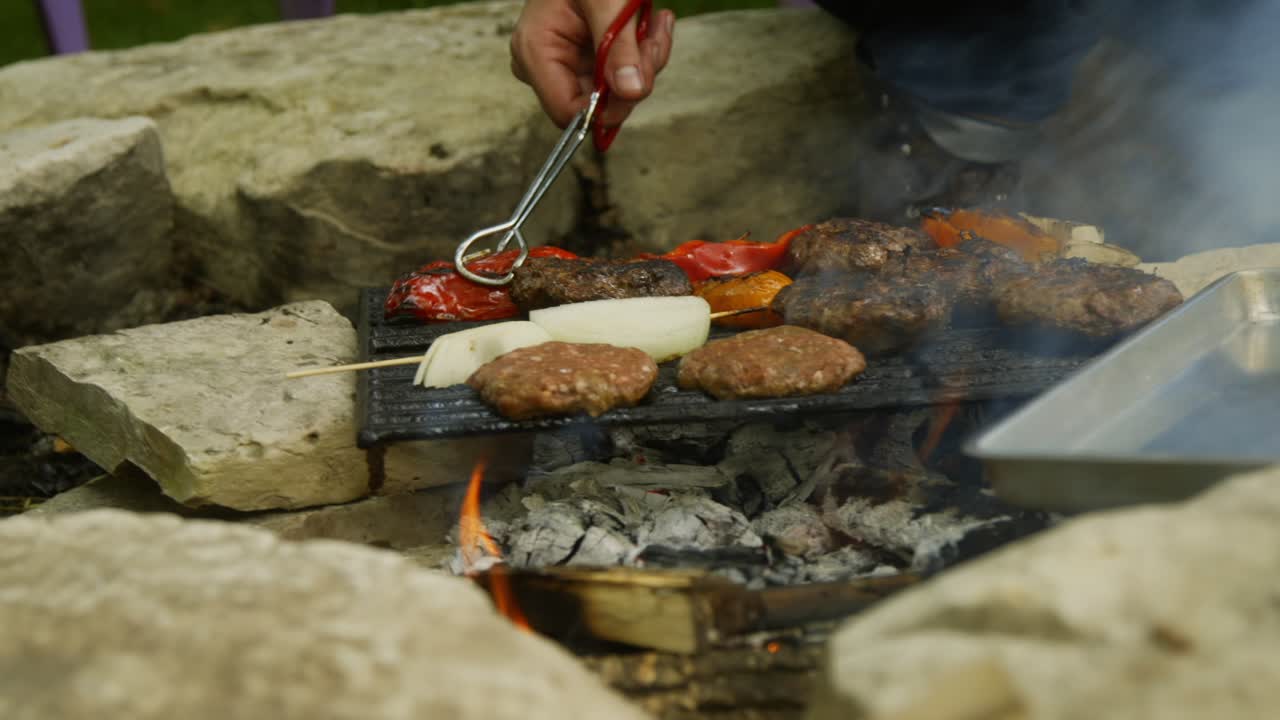 un hombre mueve los pimientos de una parrilla y en una sartén de hoja afuera