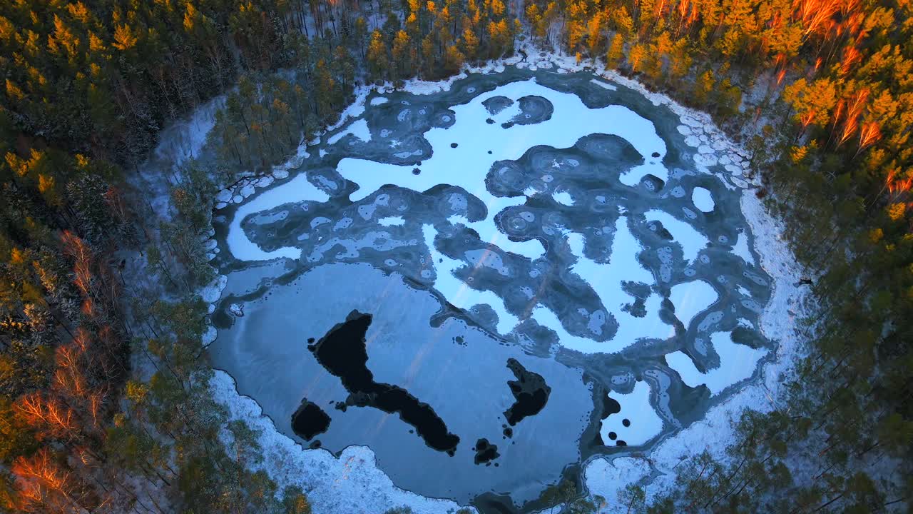 A frozen pond in a snowy forest with a swampy, winter atmosphere, aerial view