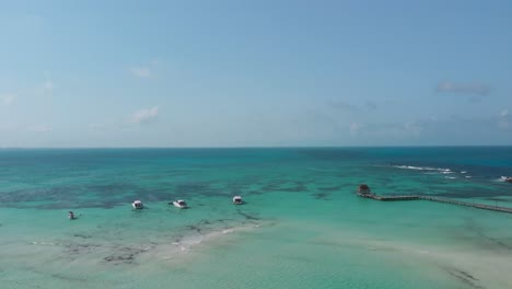 drone ascends over playa norte with boats, swimmers, coral reef shadows, and a pier in clear turquoise water