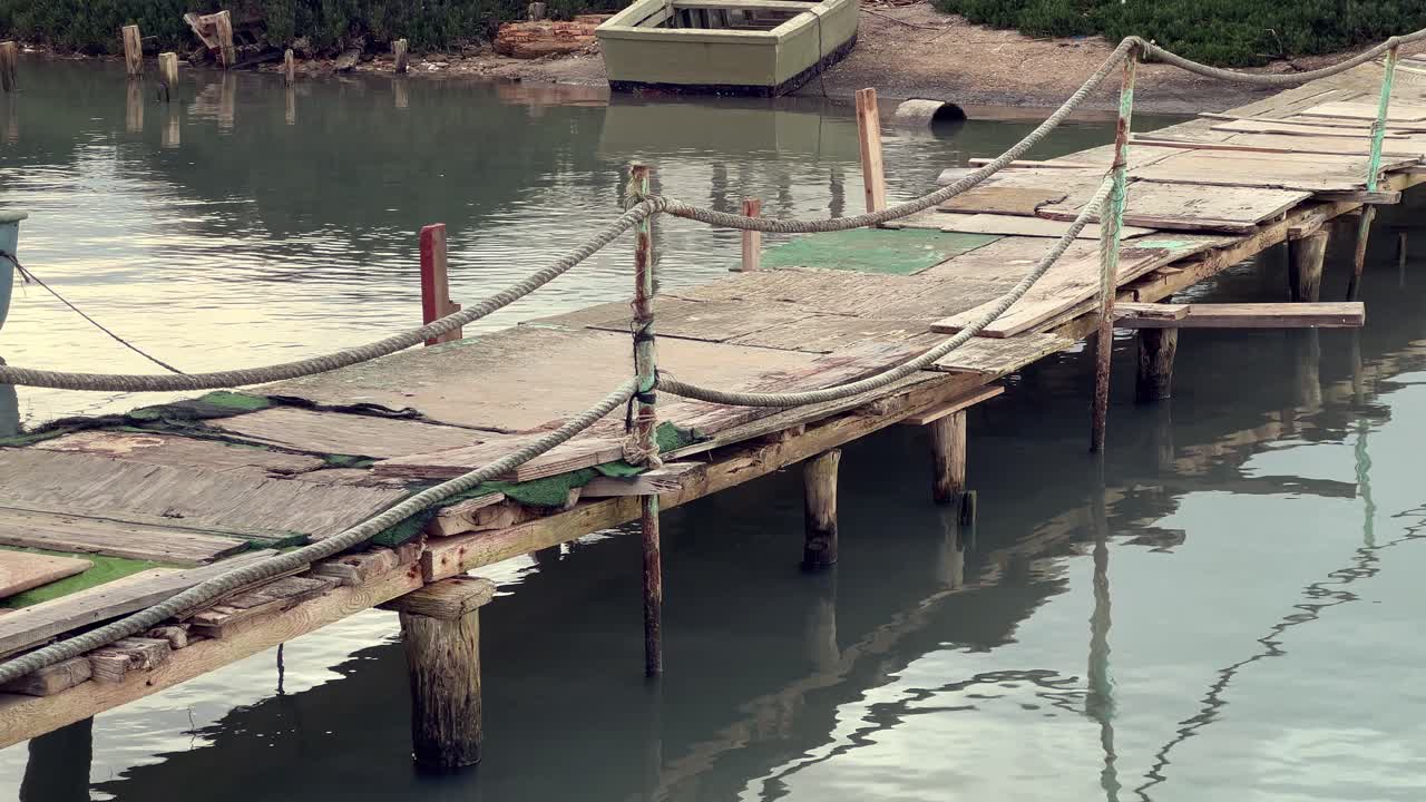 Old wooden pier is falling apart in barbate, andalusia, spain, showing signs of decay and neglect with broken planks and weathered ropes