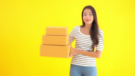 young woman holding three unmarked boxes in front of solid yellow background