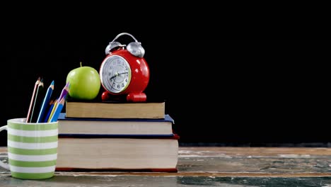 apple and alarm clock on book stack with color pencils on table