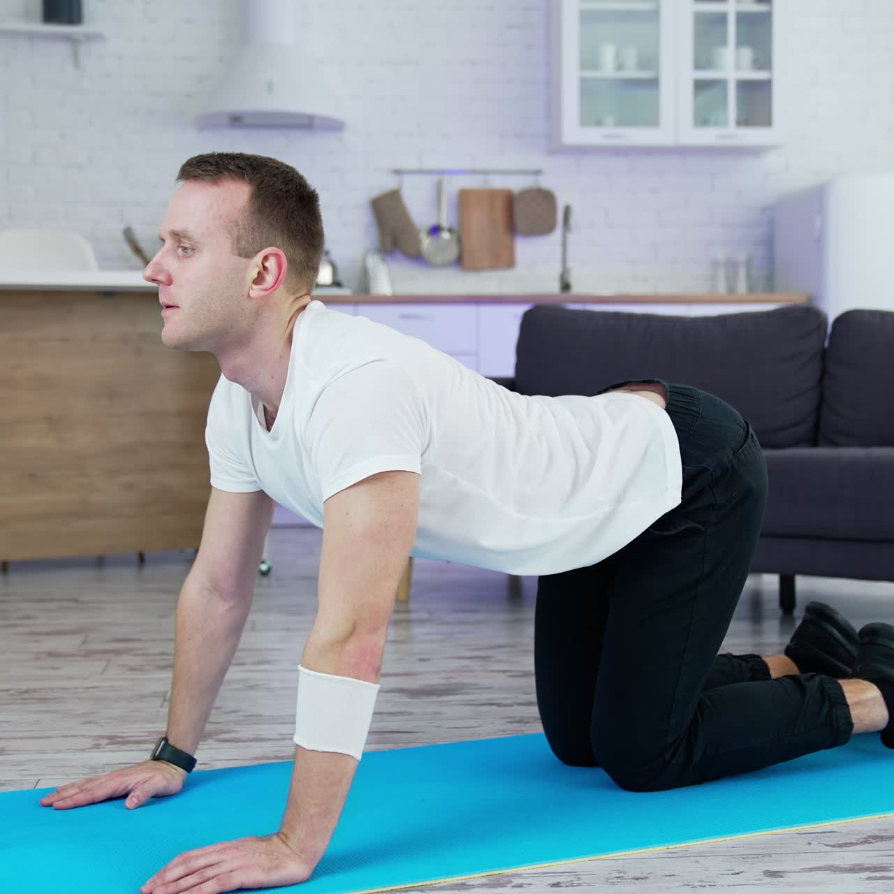 Guy doing his workout at home. Young man on a mat doing exercise of flexion and extension his back on kitchen background. Training during lockdown