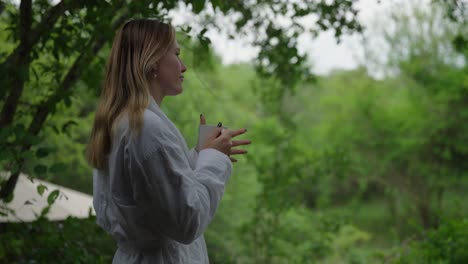 A-woman-standing-in-a-robe-drinking-coffee-in-a-green-outdoor-setting-on-safari