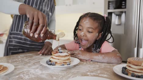 happy african american mother and daughter serving pancakes in kitchen, slow motion