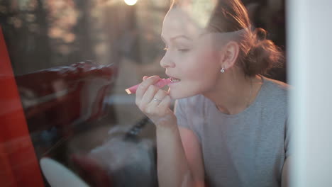 Through-the-window-portrait-of-girl-making-her-lips-shine