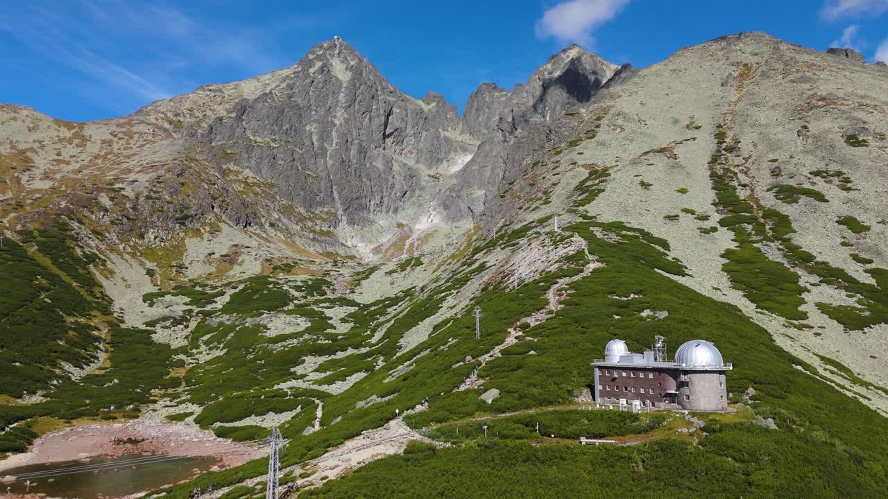 Slovakya Yüksek Tatralar'da, etkileyici Alp dağ zirvelerinin altındaki astronomik kubbeyi ortaya çıkaracak şekilde Skalnaté Pleso Gözlemevi'ne doğru drone kaydırması.