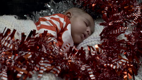 adorable cute 2 month old indian baby boy in festive outfit sleeping surrounded by red and silver tinsel