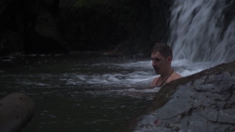 un joven nadando y relajándose en el agua fría que fluye de las hermosas cascadas - plano general