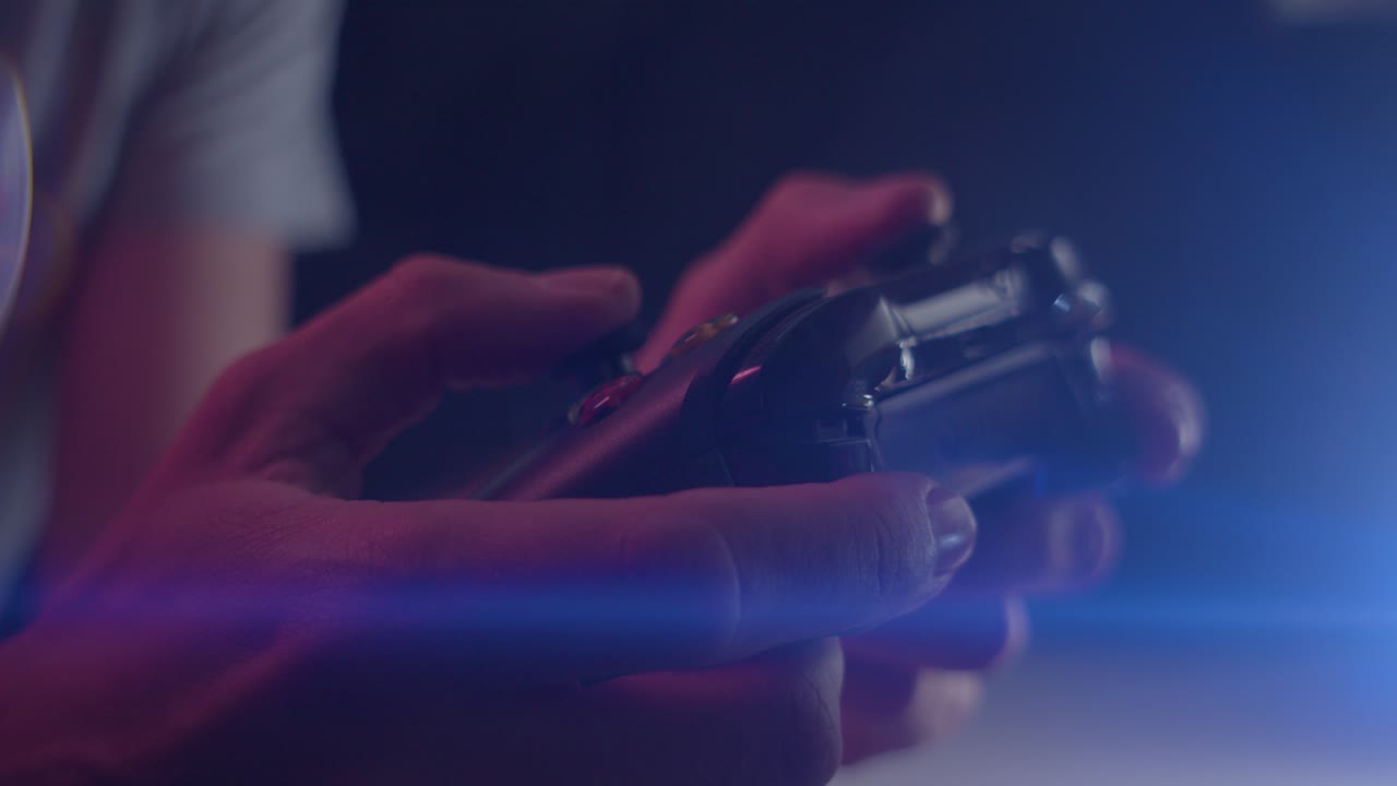 Playing video games in a darkened room with an anamorphic lens flare on a controller triggers playing slowly close up