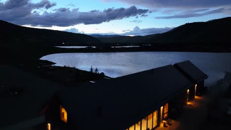 Summit-Sky-Ranch-Lake-Bootshaus-In-Silverthorne,-Colorado-Während-Der-Blauen-Stunde-Mit-Warmer-Beleuchtung-Im-Bootshaus-Aus-Der-Luft