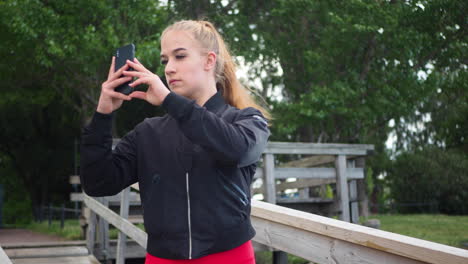 girl in sportswear walking in park and taking pictures with her smartphone