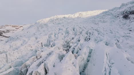 Aerial-landscape-view-over-ice-formations-in-Falljokull-glacier-covered-in-snow,-Iceland