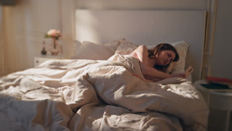 sick woman lying home in bed morning. tired awake female checking mobile phone