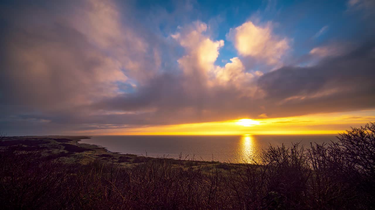lapso de tiempo de nubes rodantes sobre la costa de ameland contra cielos de puesta de sol naranja amarillo