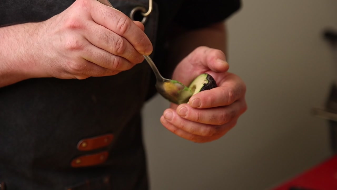 Primo piano di mani che prelevano polpa fresca di avocado con un cucchiaio