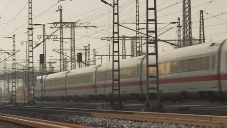 high-speed train speeding through a station with a complex network of electric lines