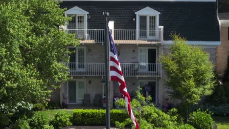 panoramic view of an american flag gently blowing in the breeze in a courtyard in front of an apartment complex on a clear summer day