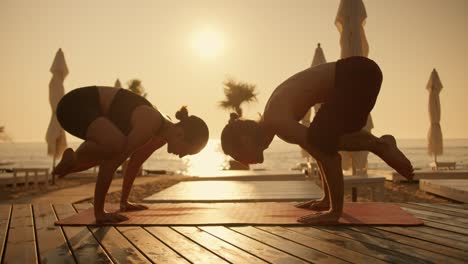 a guy and a girl are doing yoga and doing a bird pose on a red mat on a sunny beach during sunrise. combination of acrobatics