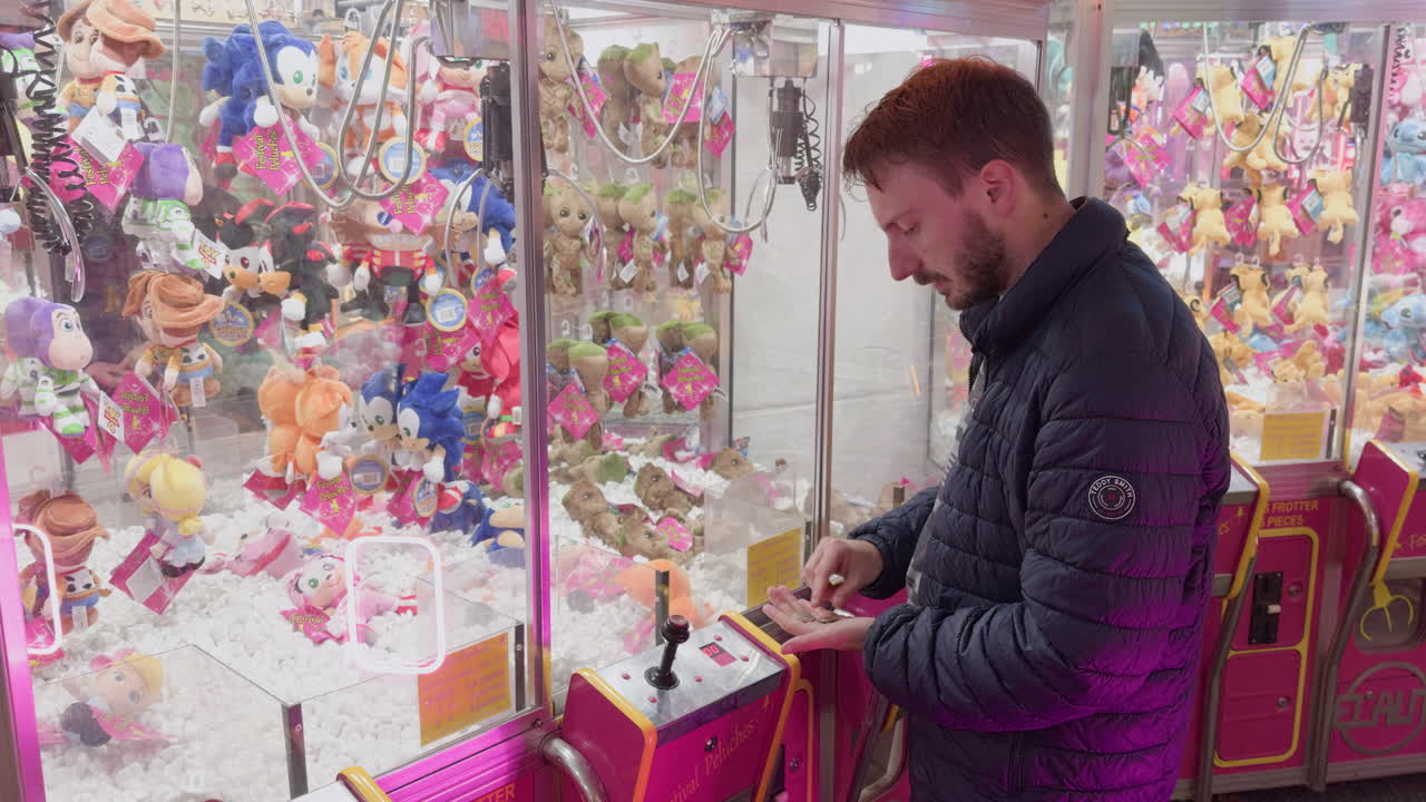 Man using claw machine at night funfair in Montrichard Val de Cher surrounded by plush toys