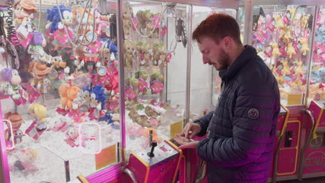 man using claw machine at night funfair in montrichard val de cher surrounded by plush toys