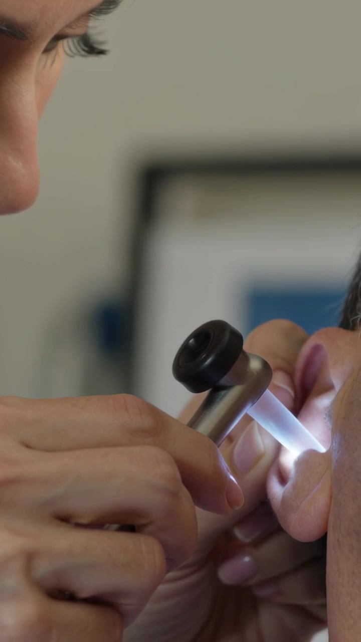 Video verticale: LED che si attiva, clinico in camice chiaro che esamina l'orecchio destro con un otoscopio in clinica.