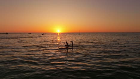 Aerial-tracking-shot-of-a-couple-paddleboarding-at-Iquique-during-sunset