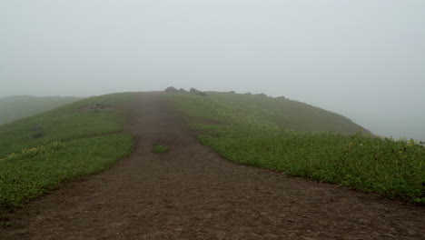 Tilting-down-shot-of-a-foggy-hill-with-a-dirt-path-in-the-foreground,-Lomas-de-Manzano,-Pachacamac,-Lima,-Peru