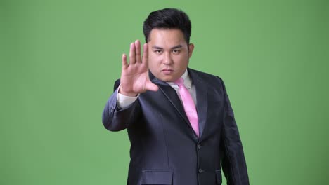 young handsome overweight asian businessman against green background