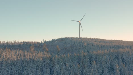 aerial - turbina eólica al amanecer en un bosque nevado en suecia, tiro amplio hacia adelante