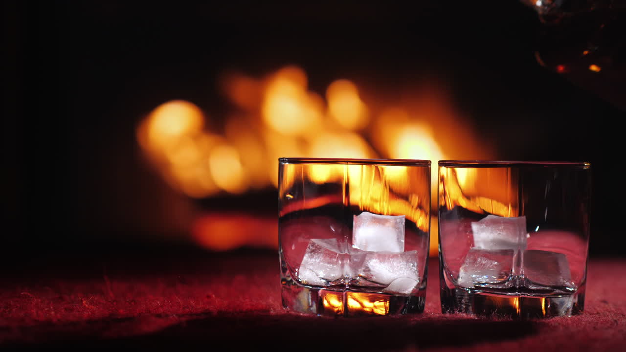 벽난로 뒤에 얼음이 든 유리잔에 위스키를 붓는다