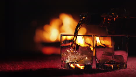 whiskey is poured into a glass with ice on the background of the fireplace