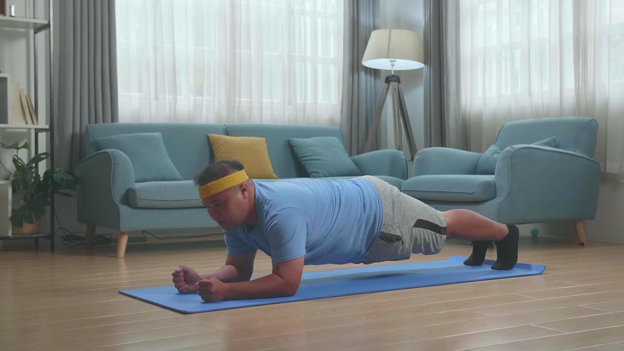 hombre gordo asiático haciendo yoga en el antebrazo en una postura de tabla en la alfombra en casa