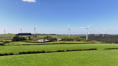 Wind Turbines, Cornasaus, County Cavan, Ireland, April 2023. Drone pushes forward and ascends above the rural fields with a farm house in center and windmills spinning in background on a sunny day.