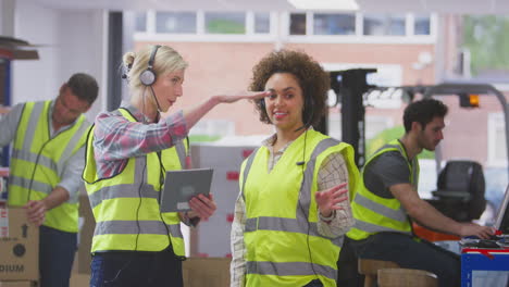 two female workers wearing headsets in logistics distribution warehouse using digital tablet