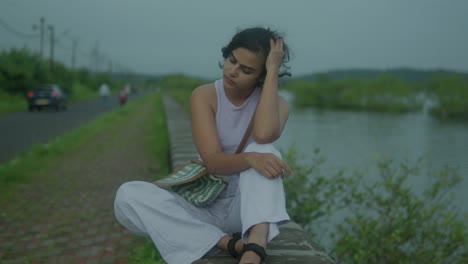 Beautiful,-young-female-running-her-fingers-through-her-hair-and-thinking-deeply-whilst-sitting-road-side