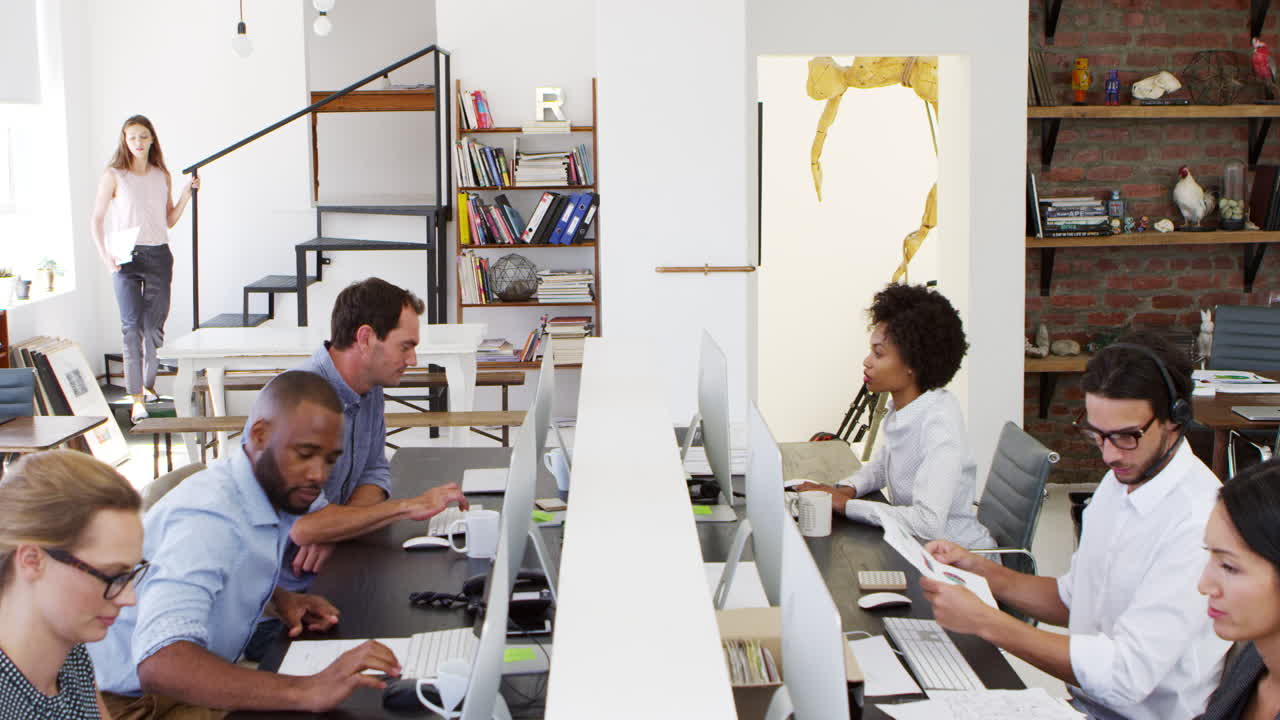 Colleagues sit using computers in a busy open plan office
