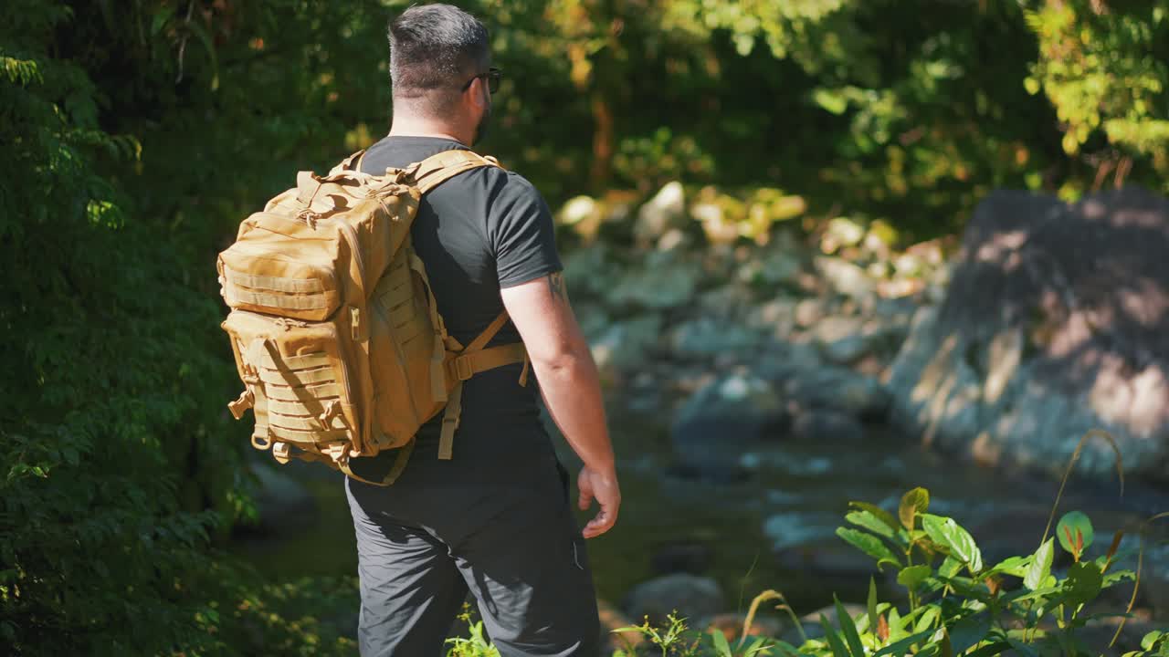 un joven excursionista masculino que atraviesa un río de montaña rodeado de rocas y árboles