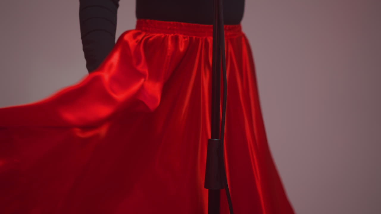 cantante sin rostro en vestido negro y rojo con gracia sosteniendo y girando la vibrante tela roja del vestido en un entorno de estudio. el movimiento dinámico y los colores ricos crean un dramático