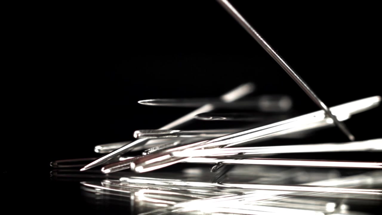 Slow Motion Close-Up of Sewing Needles Falling on a Black Reflective Surface