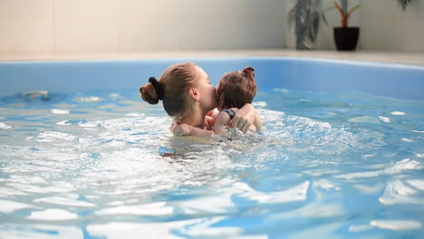 cute blonde toddler in protective glasses is diving under the water together with his mother in the swimming pool trying to take out his toy. his mother is teaching him how to swim. an underwater shot.