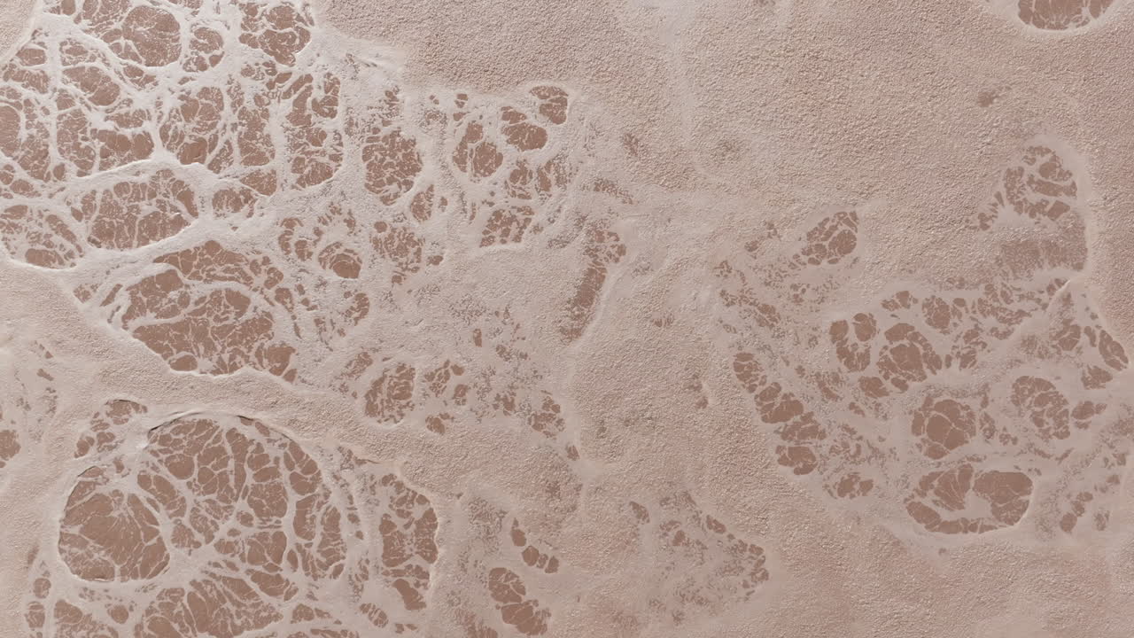 A pale, beige-tinted aerial view shows swirling foam patterns within a settling basin, highlighting early stages of the treatment cycle
