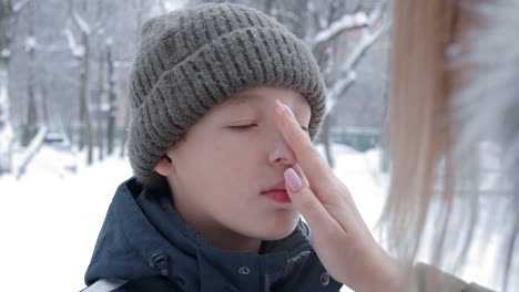 boy getting winter skin care from mom applying face cream