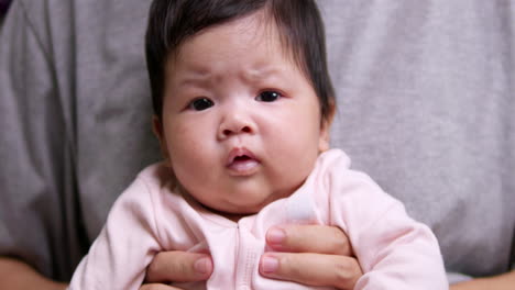 a newborn baby is furrowing her brows and squirming while her mother is holding her down on her lap.