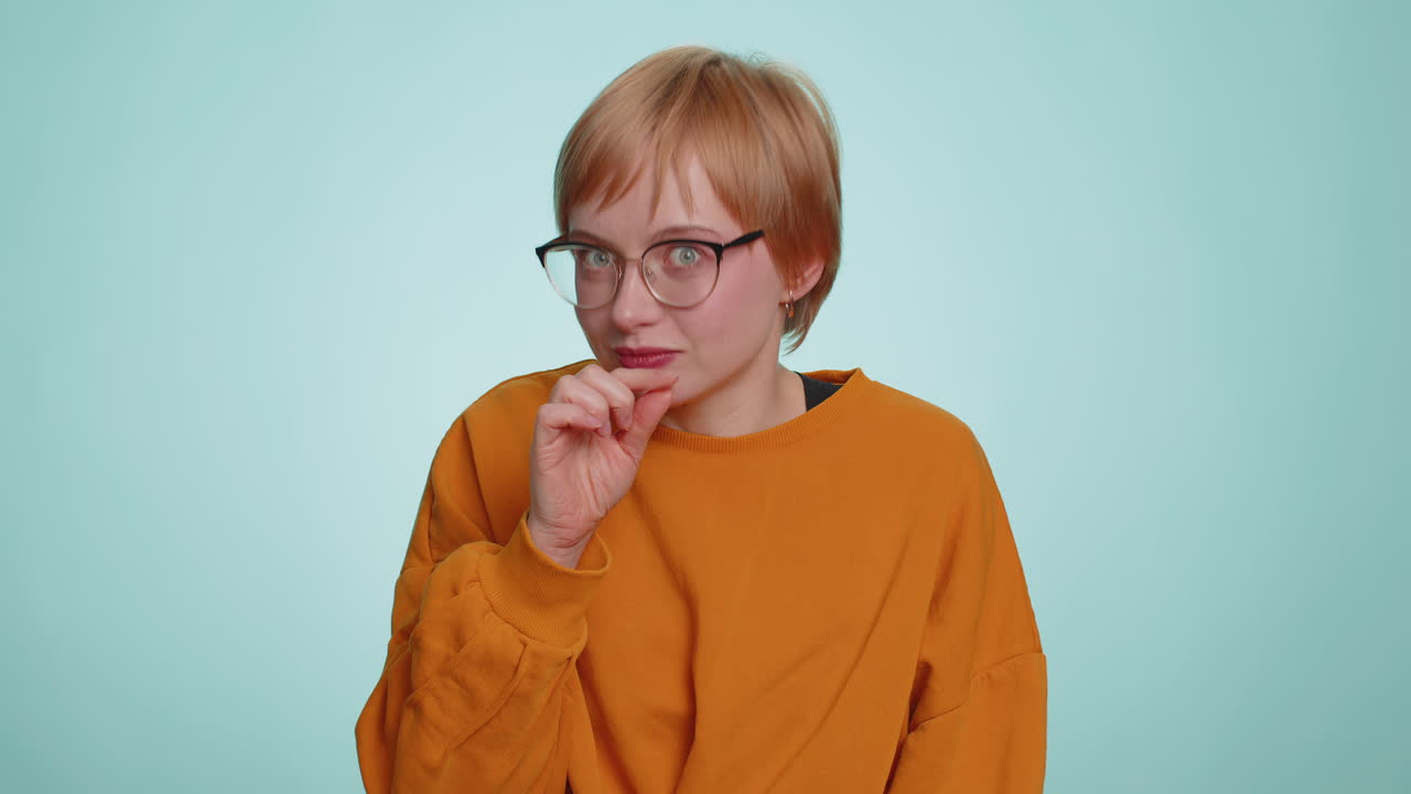 Young woman presses finger to lips makes silence gesture sign do not tells secret stop gossip